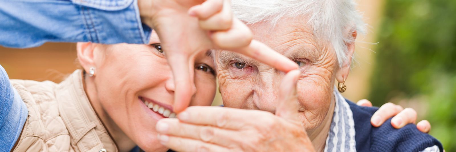 Eine junge und eine ältere Dame stehen lächelnd zusammen und halten mit den Händen ein Quadrat in die Fotokamera